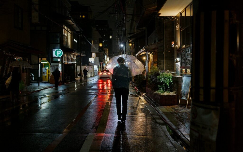 A person walks down a wet street at night.