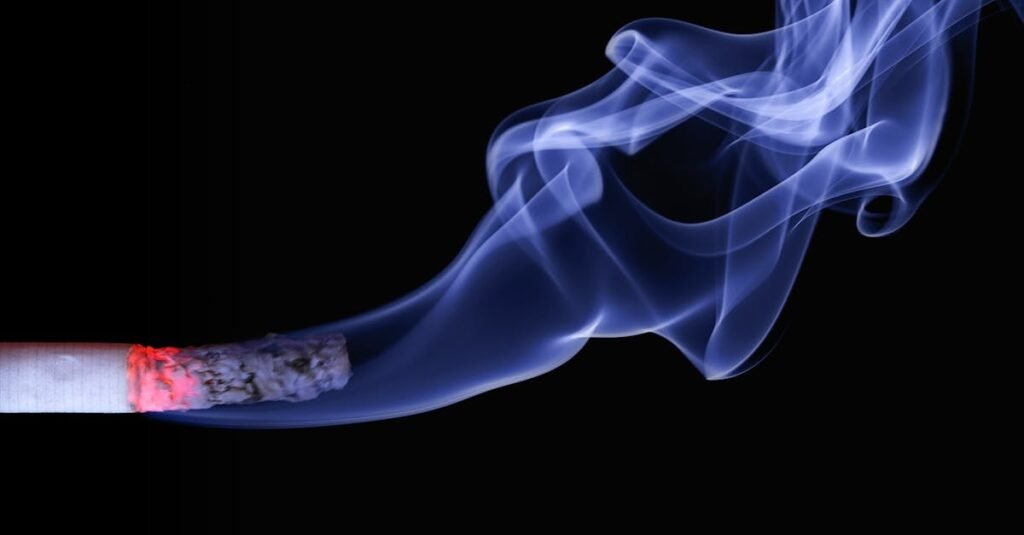 Detailed close-up of a cigarette with glowing ember and swirling smoke on a black background.