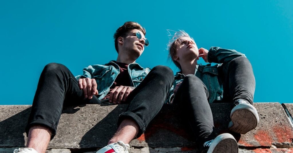 Two young people sitting on a stone wall under a vibrant blue sky, enjoying a sunny day together.