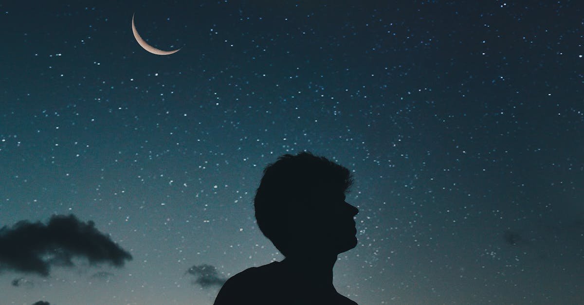 A lone silhouette stands beneath a crescent moon and starry sky, evoking a sense of solitude and wonder.