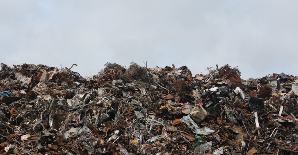 A large pile of scrap metal and waste at a landfill against a cloudy sky.