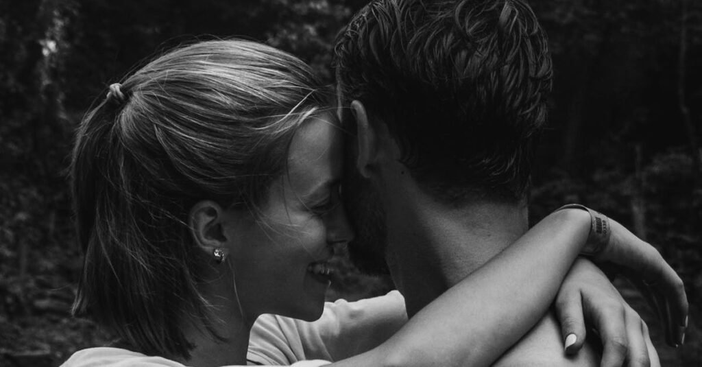 A couple shares an intimate embrace outdoors, captured in black and white.