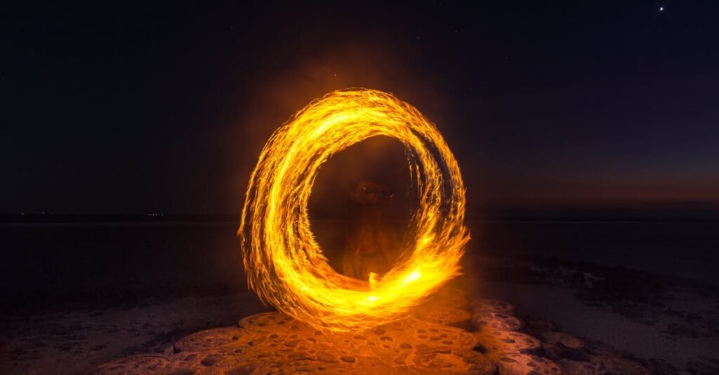 Captivating long exposure shot of a fire dancer creating fiery circles on a serene beach at night.