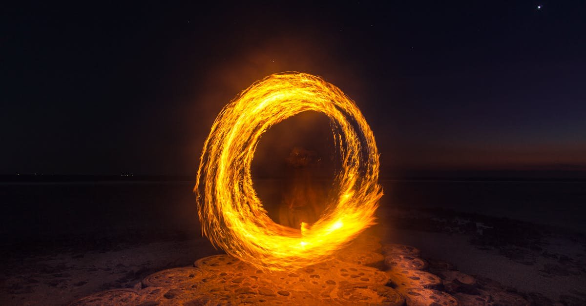 Captivating long exposure shot of a fire dancer creating fiery circles on a serene beach at night.