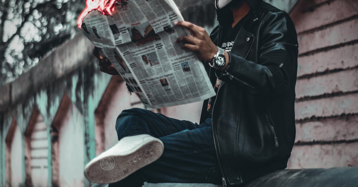 A person wearing a mask reads a flaming newspaper on an urban street, creating a surreal and mysterious scene.