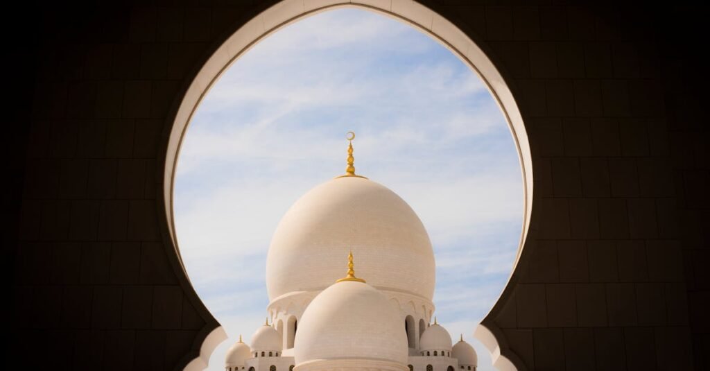 Captivating view of white domes of Sheikh Zayed Grand Mosque through an archway against the blue sky.