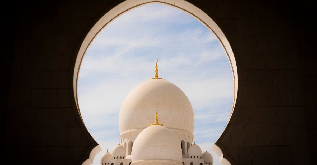 Captivating view of white domes of Sheikh Zayed Grand Mosque through an archway against the blue sky.