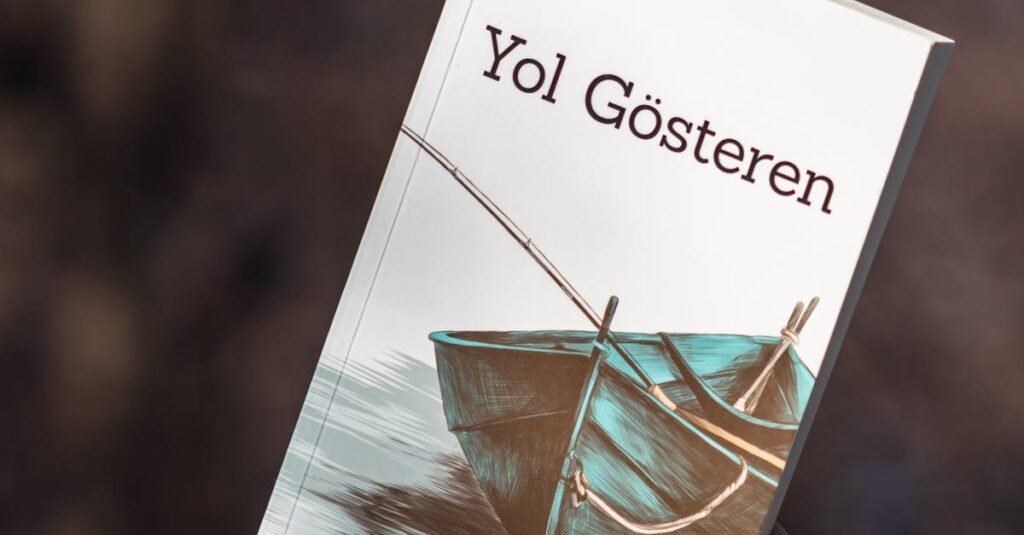 A person holding the book 'Yol Gösteren' against a blurred outdoor background, featuring an orange sweater.
