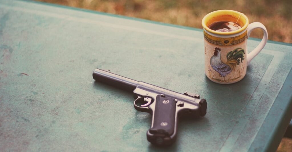 A handgun and rooster-themed mug with tea on a green outdoor table.