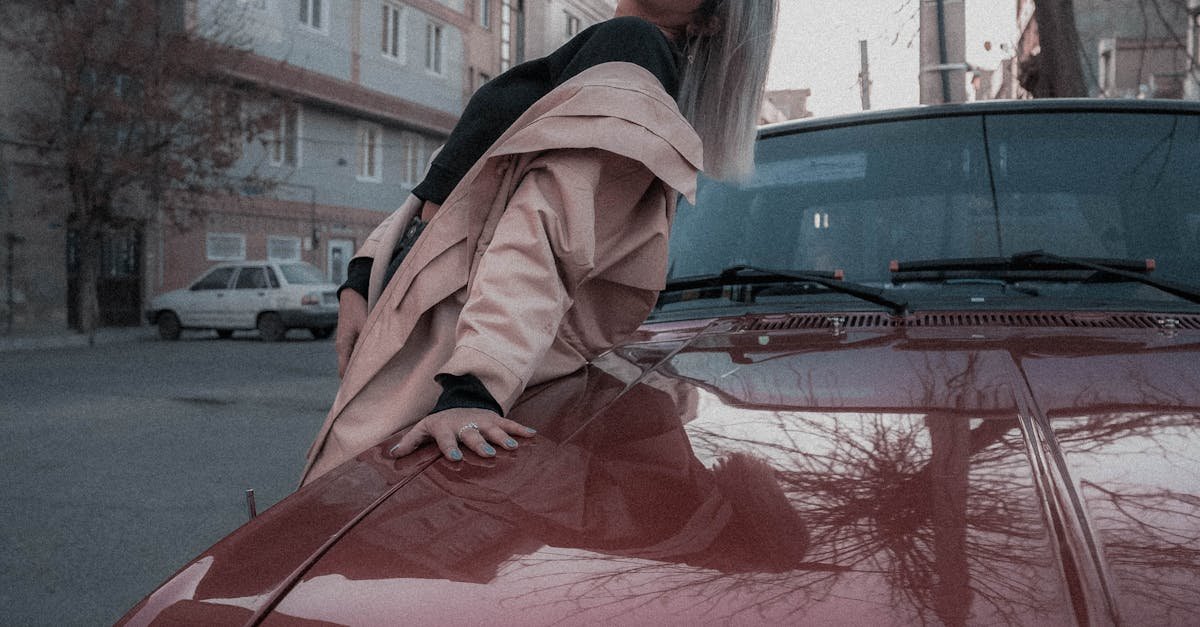 Fashionable woman in sunglasses resting on vintage red car in urban setting.