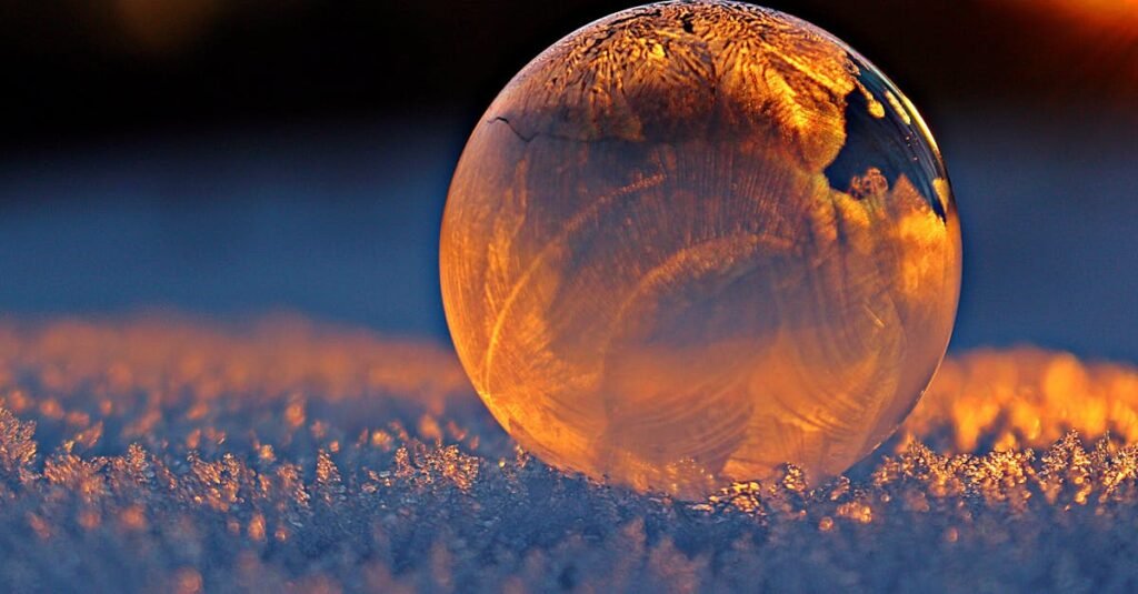 Close-up shot of a frozen bubble with warm reflections resting on a snowy surface at twilight.