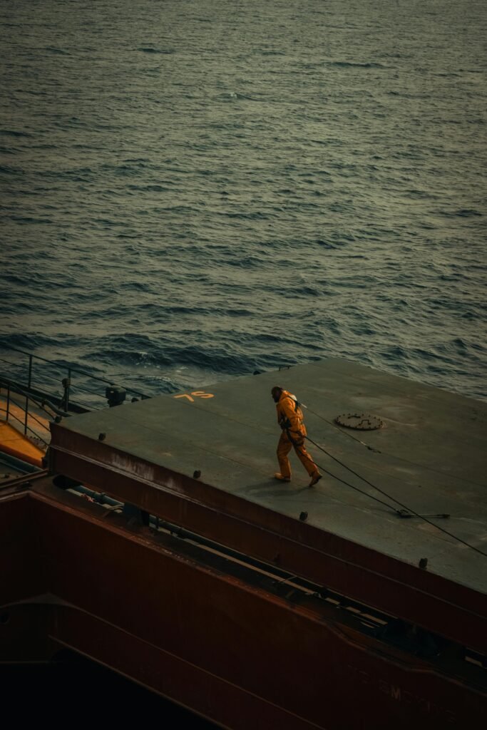A solitary worker on a ship deck with an expansive ocean view, captured during the day.