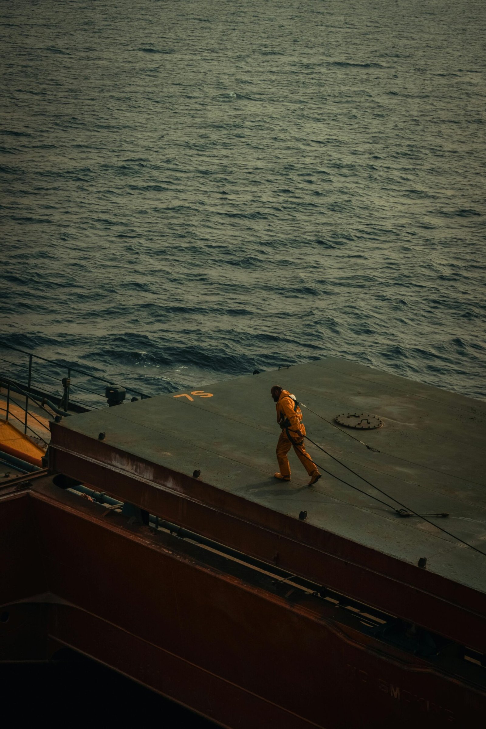 A solitary worker on a ship deck with an expansive ocean view, captured during the day.