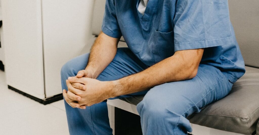 A male doctor in hospital attire sitting pensively, representing healthcare challenges.