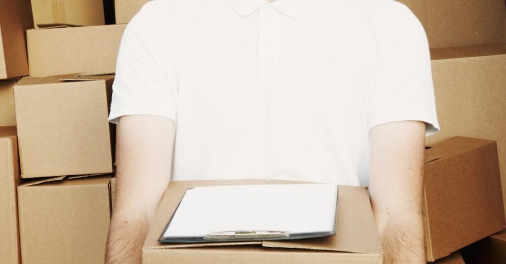 A deliveryman in a cap holding a box standing in front of a truck loaded with cartons.