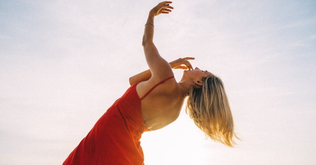 A graceful woman in a red dress dances outdoors against a bright sky background.