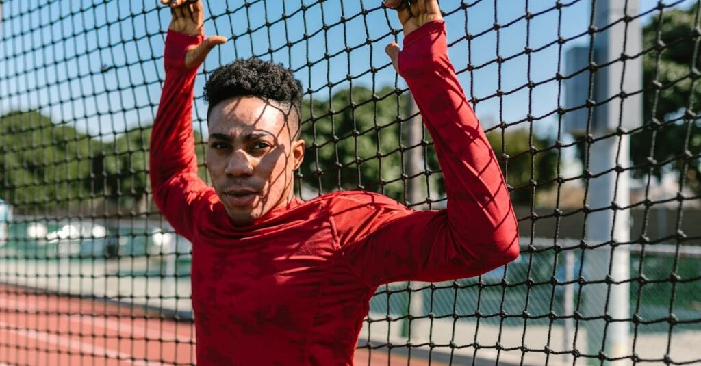 An athlete in red sportswear leans on a net on an outdoor track.