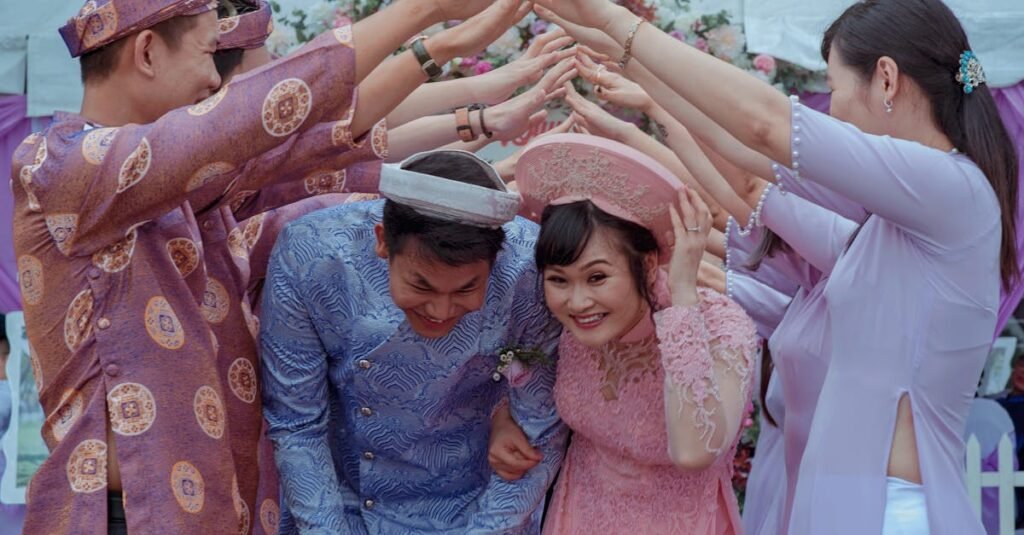 Happy Vietnamese couple celebrates their wedding with friends in traditional attire outdoors.