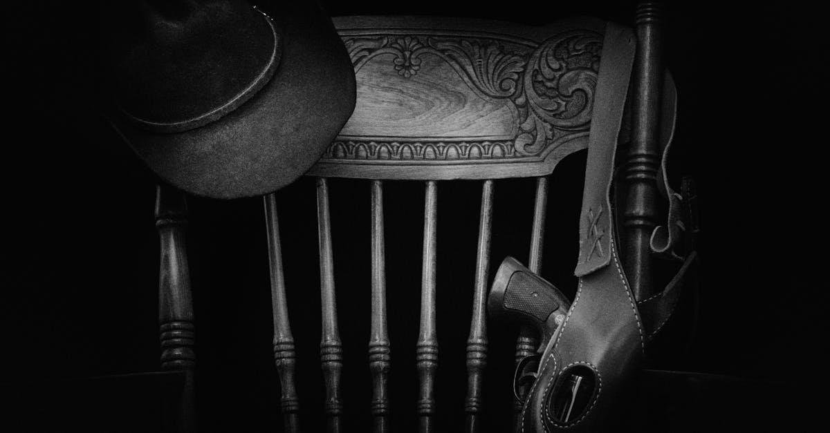 A classic western-themed black and white still life featuring a hat, wooden chair, and gun.