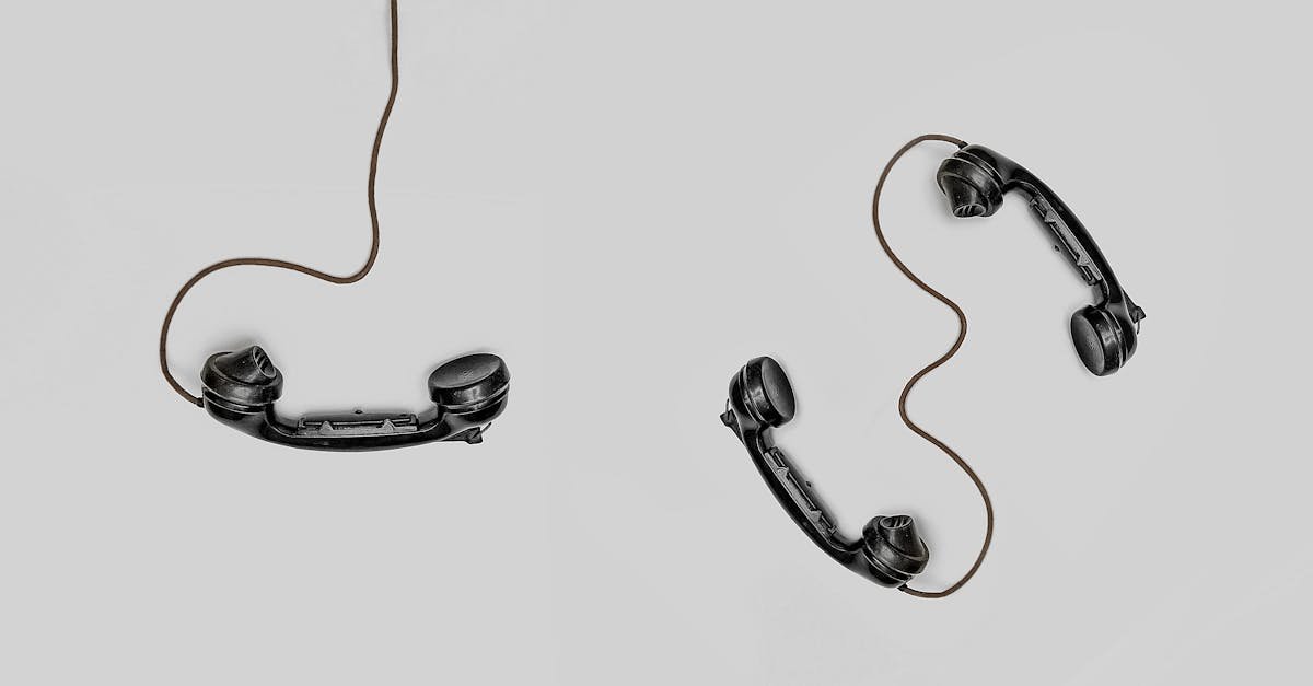 Two vintage black telephone handsets connected by cords on gray background.