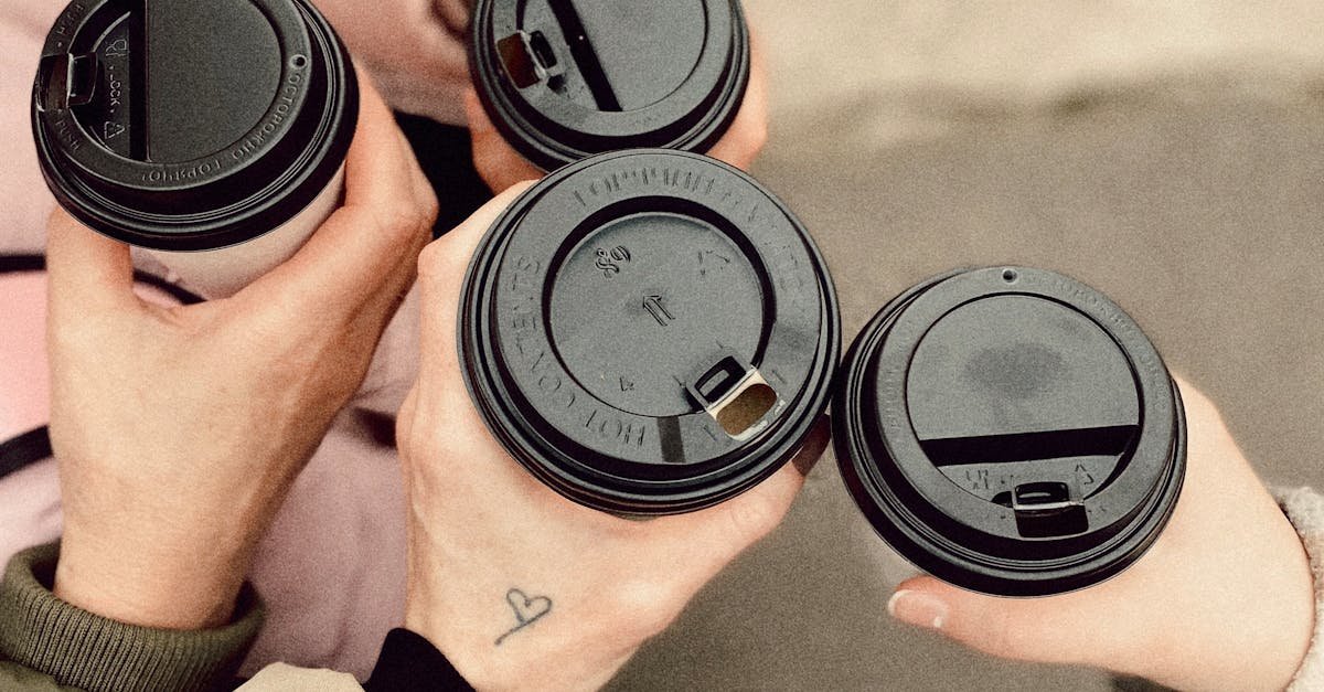 Top view of five people holding disposable coffee cups outdoors, showcasing friendship and warmth.
