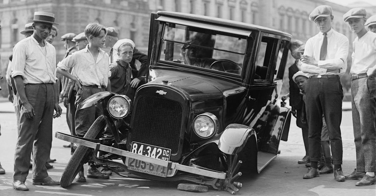 A vintage car crash attended by a group of onlookers in a 1920s urban setting.