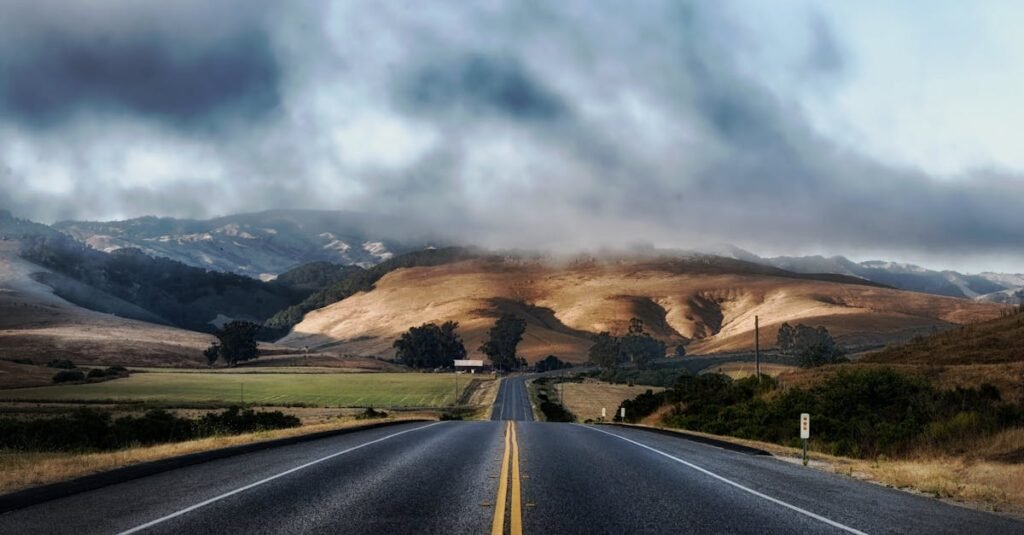 Dramatic sky over a deserted highway flanked by rolling hills, ideal for travel themes.