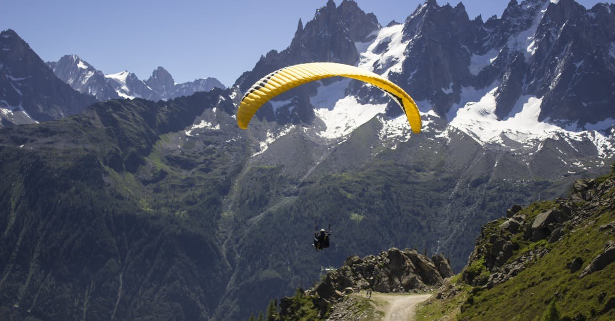 A paraglider gracefully flies over rocky mountain peaks on a sunny day, offering a sense of adventure and freedom.