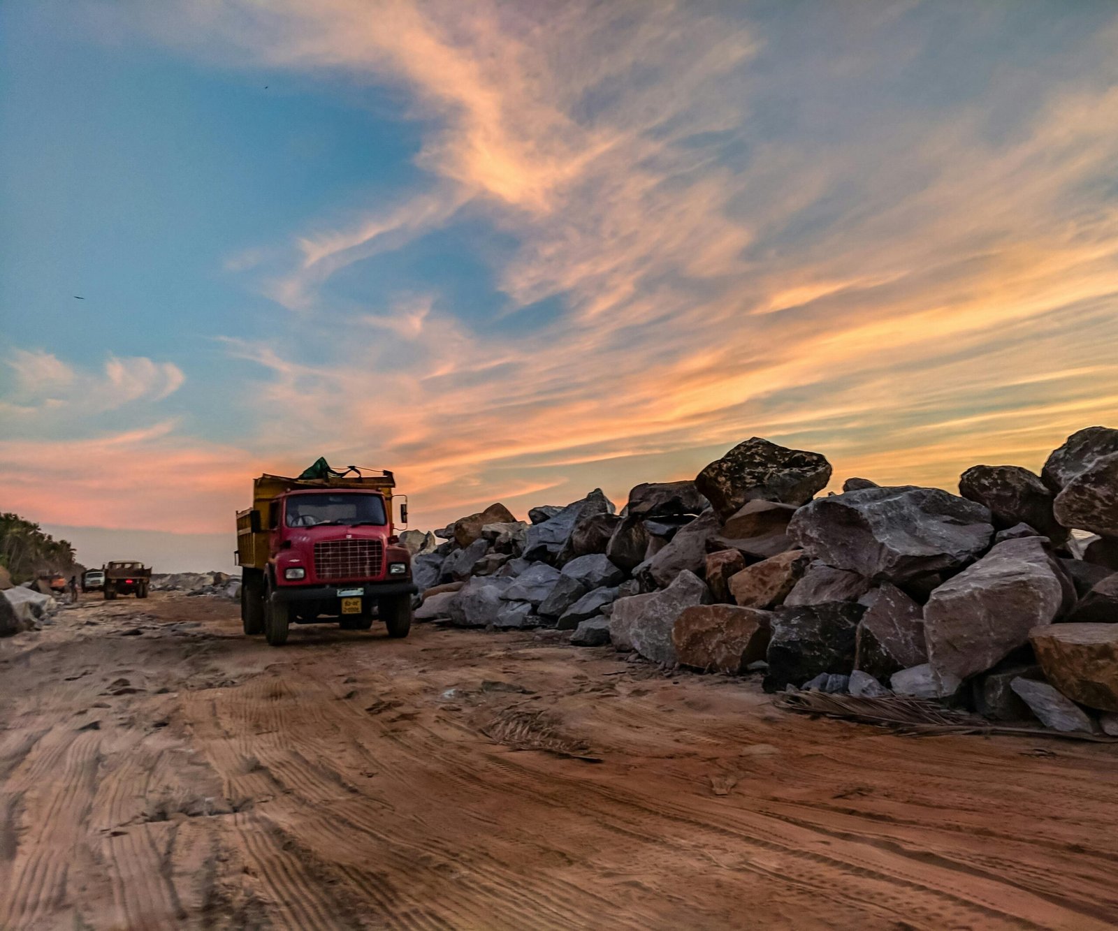 Vibrant sunset over trucks and rocks on a busy construction site, highlighting industrial work.