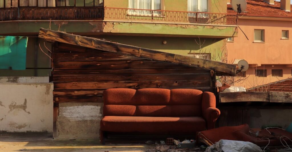 A rustic urban setting featuring an abandoned couch against a wooden wall with residential buildings in Ankara, Turkey.