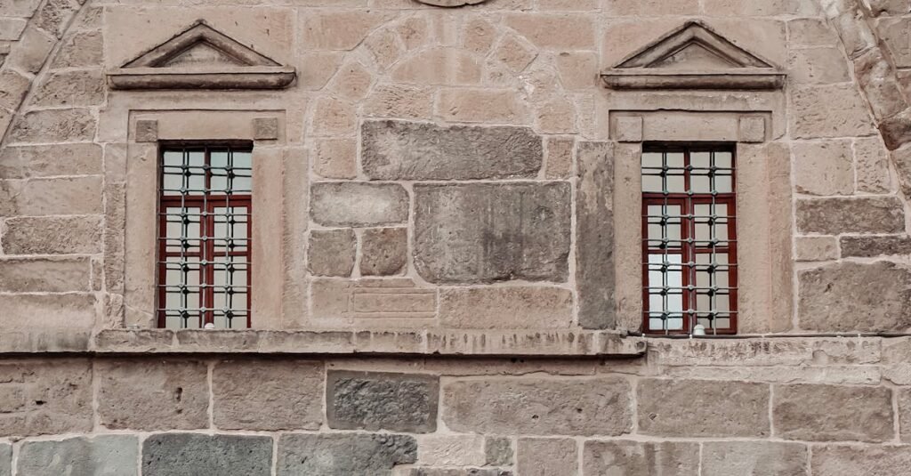 A woman in a hijab stands with a book outside a historic mosque in Kayseri, Türkiye.