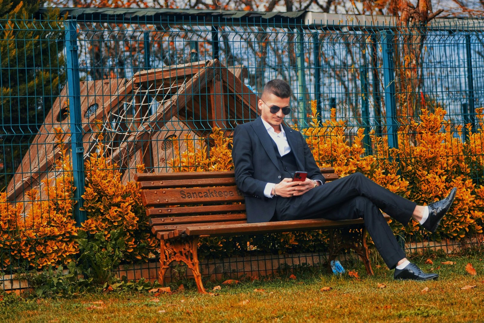 A stylish man in sunglasses sitting on a bench in autumn, using a smartphone.