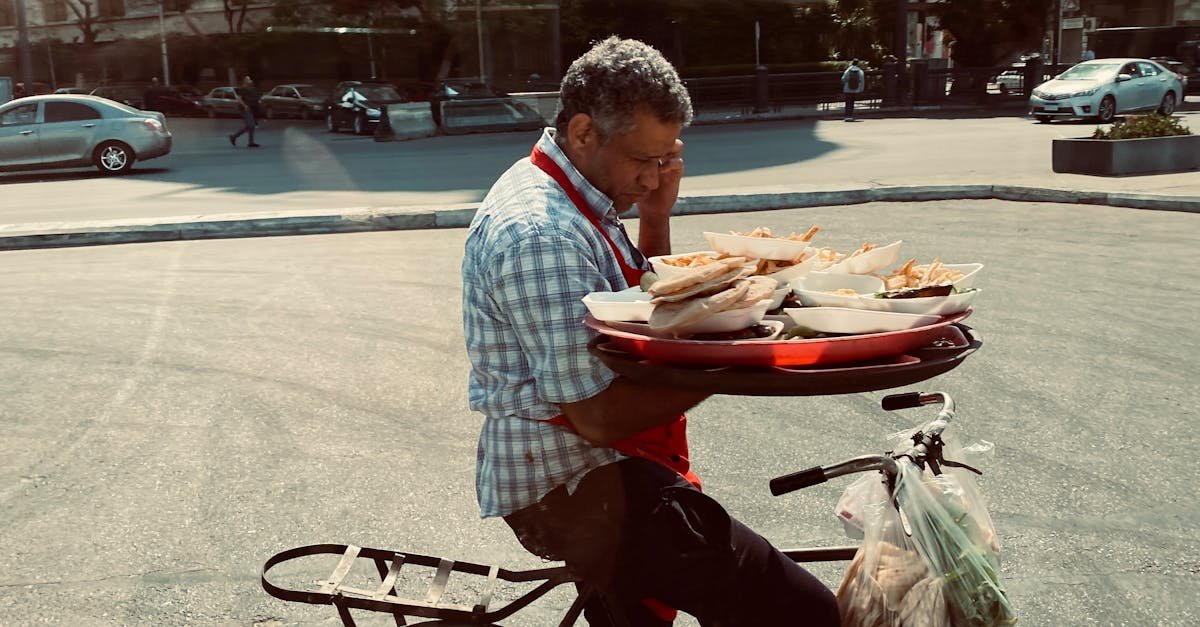 A man skillfully balances food trays on a bicycle in an urban Cairo street, showcasing daily life in the city.