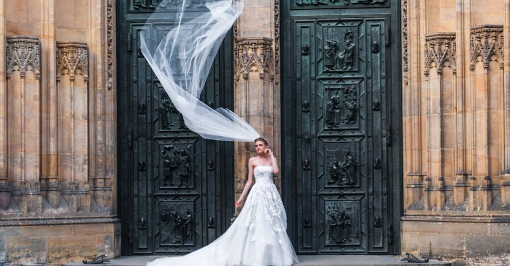 A beautiful bride poses with flowing veil in front of a gothic cathedral entrance.