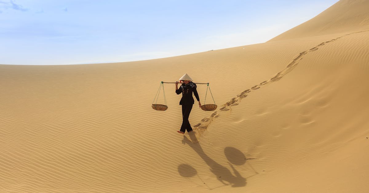 A solitary traveler crossing sand dunes, bearing baskets under a sunny sky.