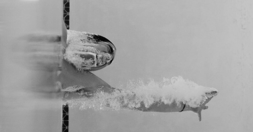 Monochrome photo of a swimmer diving underwater, showcasing motion and strength.