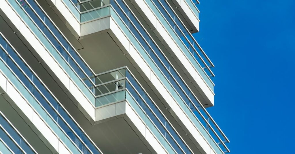Capture of a contemporary skyscraper with glass balconies against a clear blue sky.