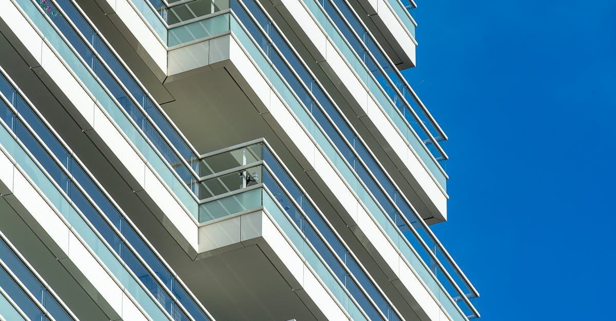 Capture of a contemporary skyscraper with glass balconies against a clear blue sky.