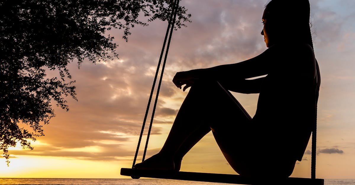 A serene sunset silhouette of a woman sitting on a swing by the seashore, evoking tranquility and reflection.