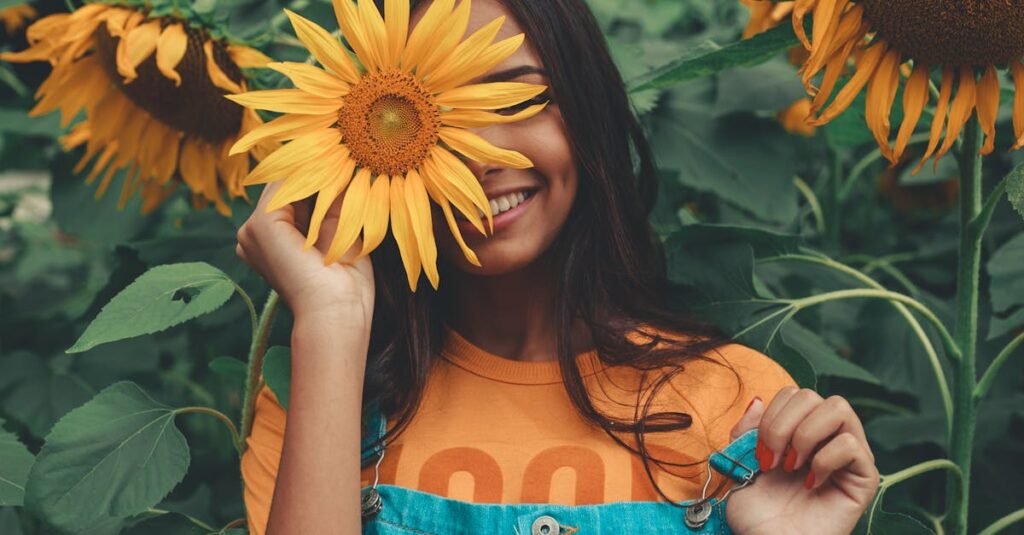 Joyful woman in denim holding sunflower among vibrant blooms in summer garden.