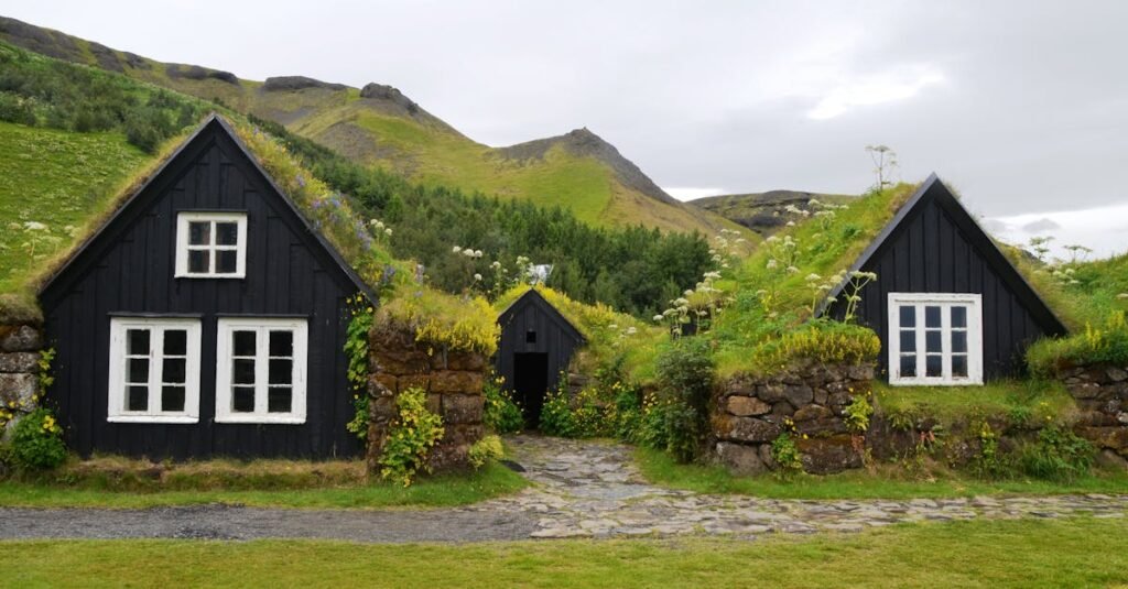 Explore the rustic charm of traditional turf roofed houses set against a lush hillside in serene countryside.