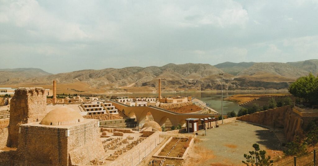 Explore the ancient ruins set against a backdrop of mountains and a winding river under a bright sky.