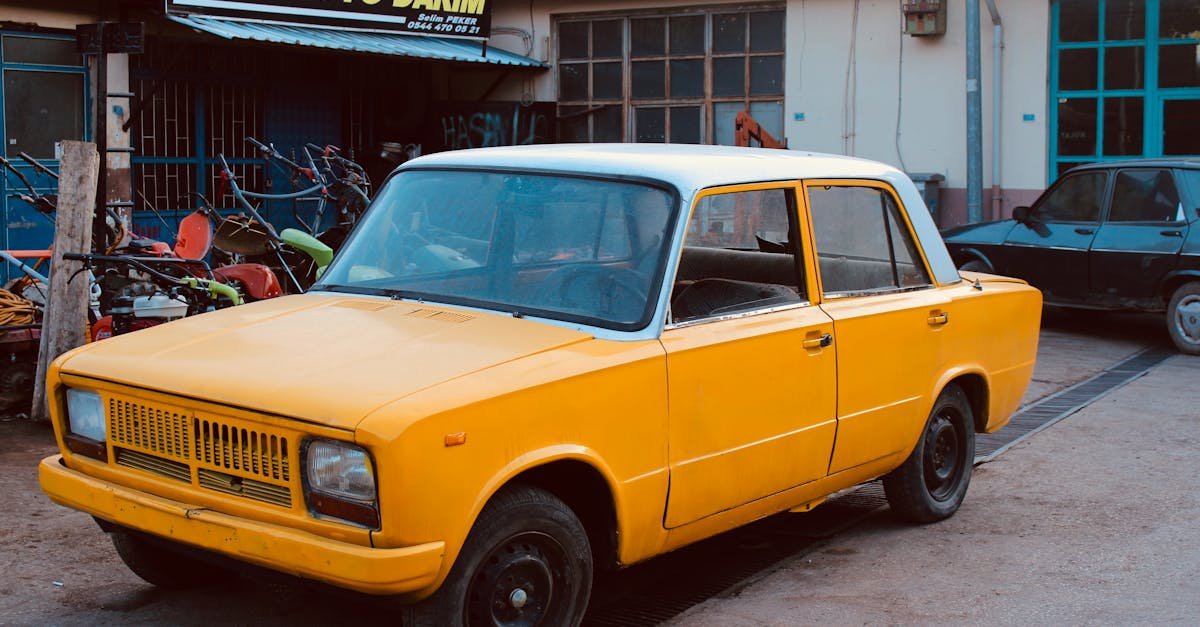A classic yellow car parked outside a local auto repair shop with tools visible.
