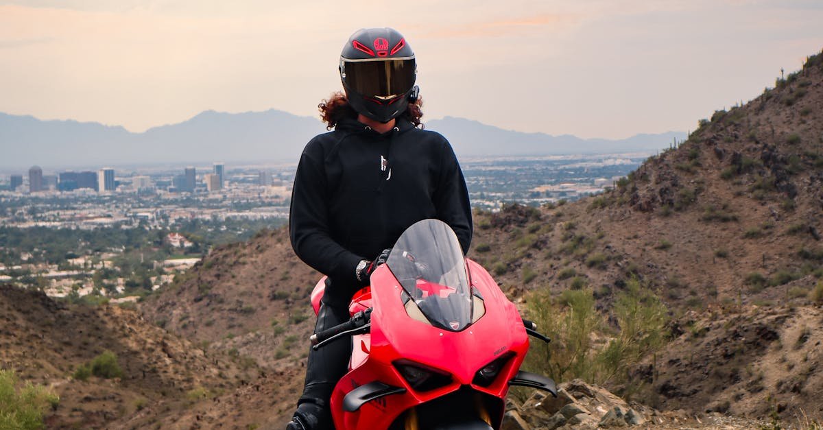 Rider in black helmet on red motorcycle with city skyline in background.