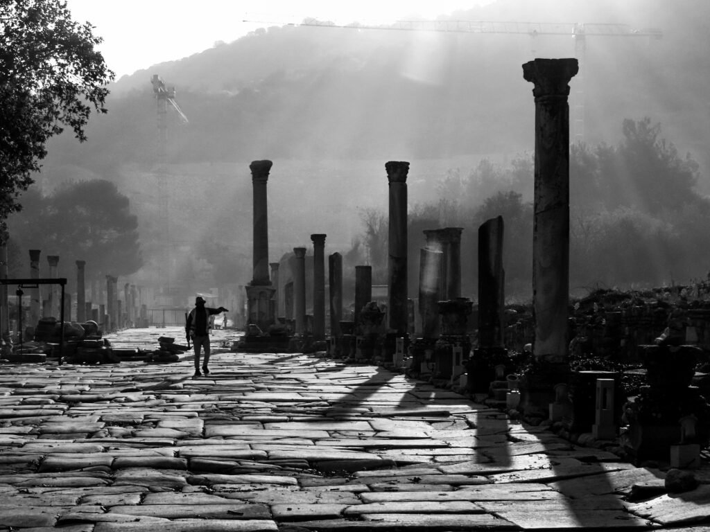 A striking black and white view of ancient ruins in Ephesus, İzmir under dramatic sunlight.