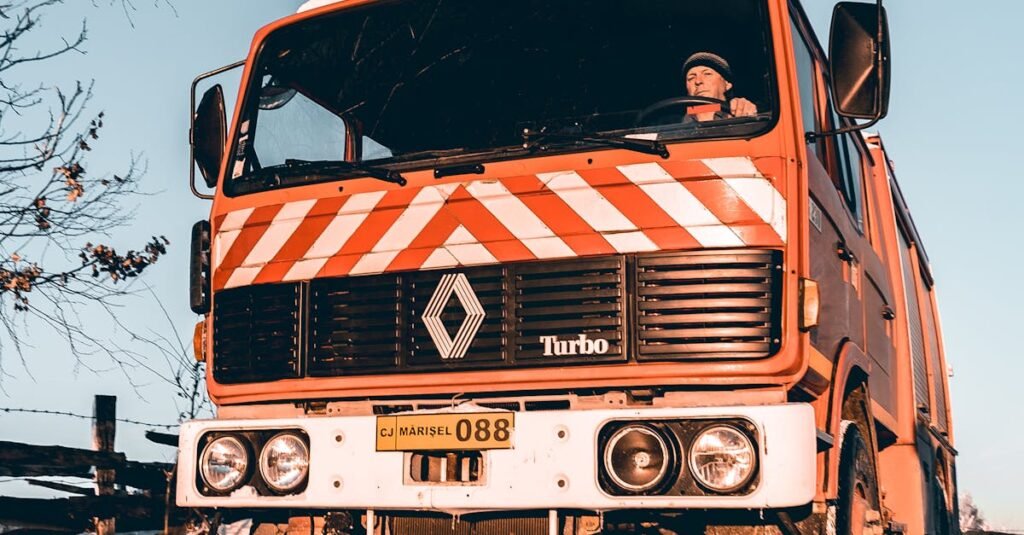 Red truck navigating a snowy road during winter with clear blue sky.