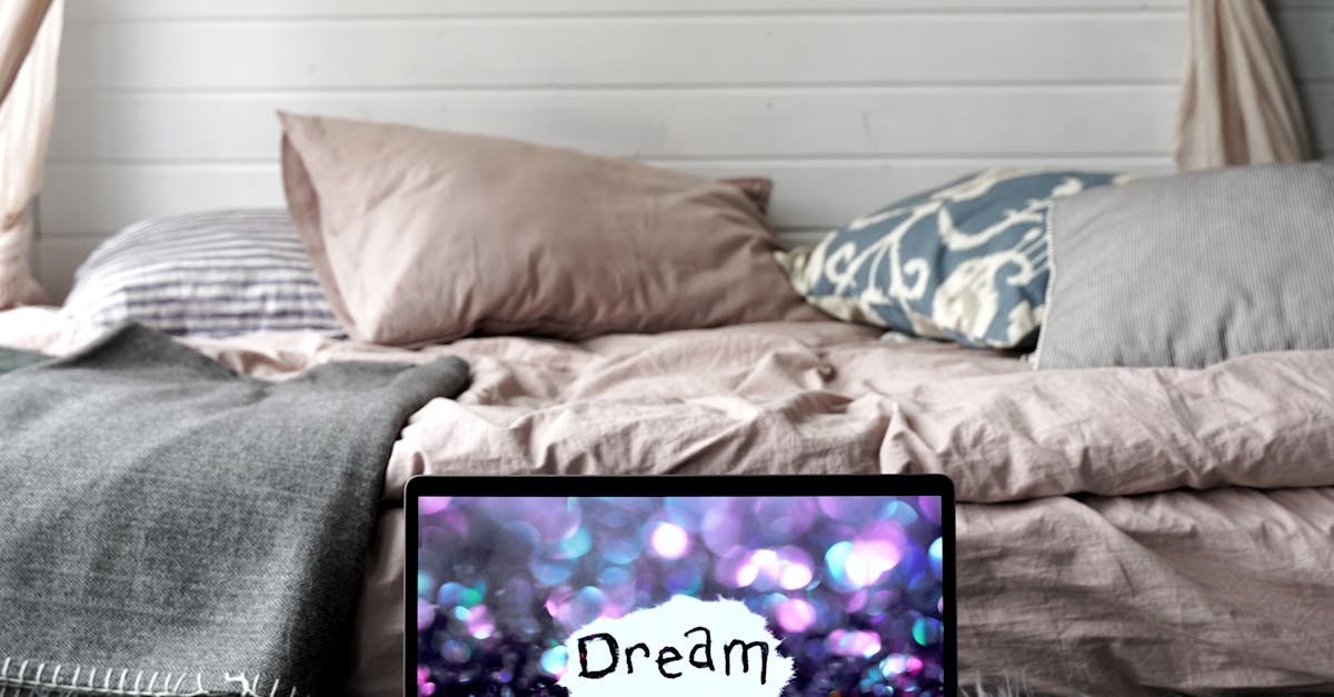 A serene bedroom with a laptop displaying 'Dream' amidst cozy pillows and soft textiles.