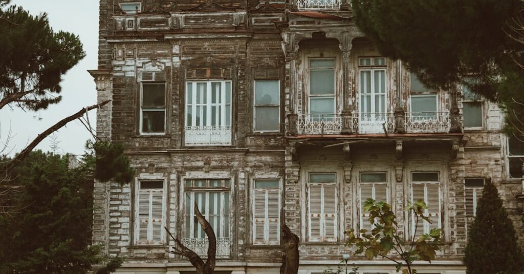 A dilapidated mansion with vintage architecture amidst a garden setting, showcasing intricate exterior details.