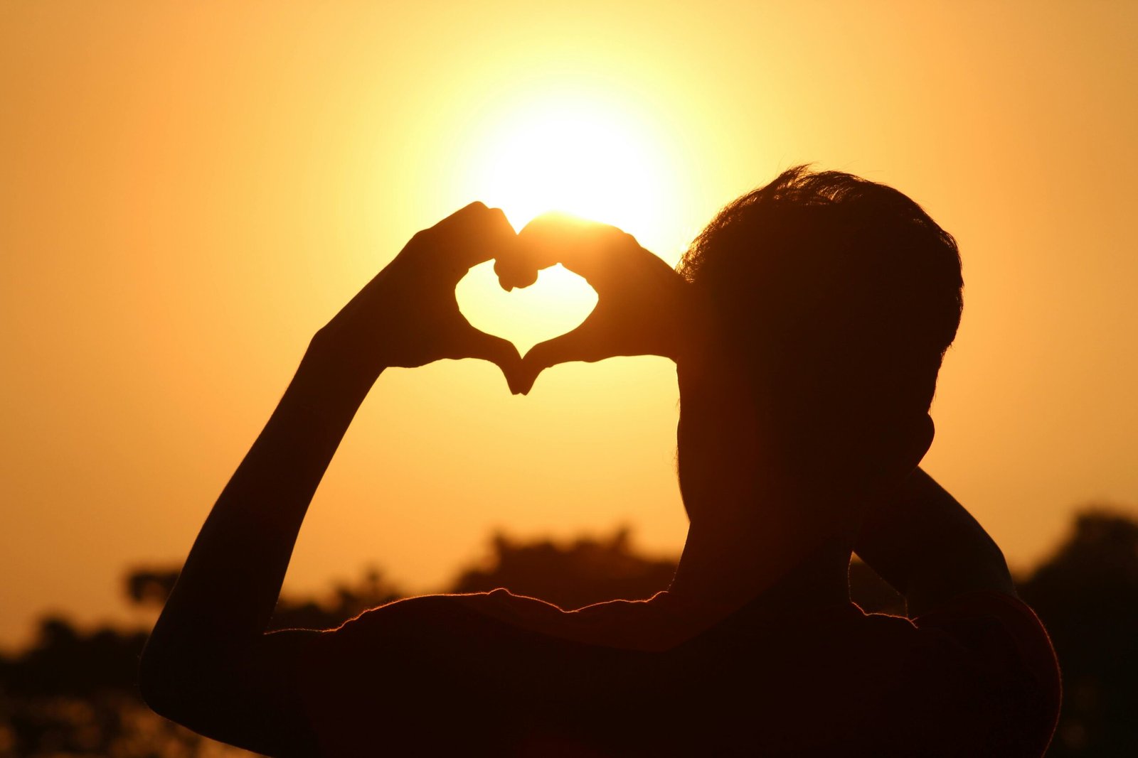A silhouette of hands forming a heart shape against a vibrant sunset in Bangladesh.