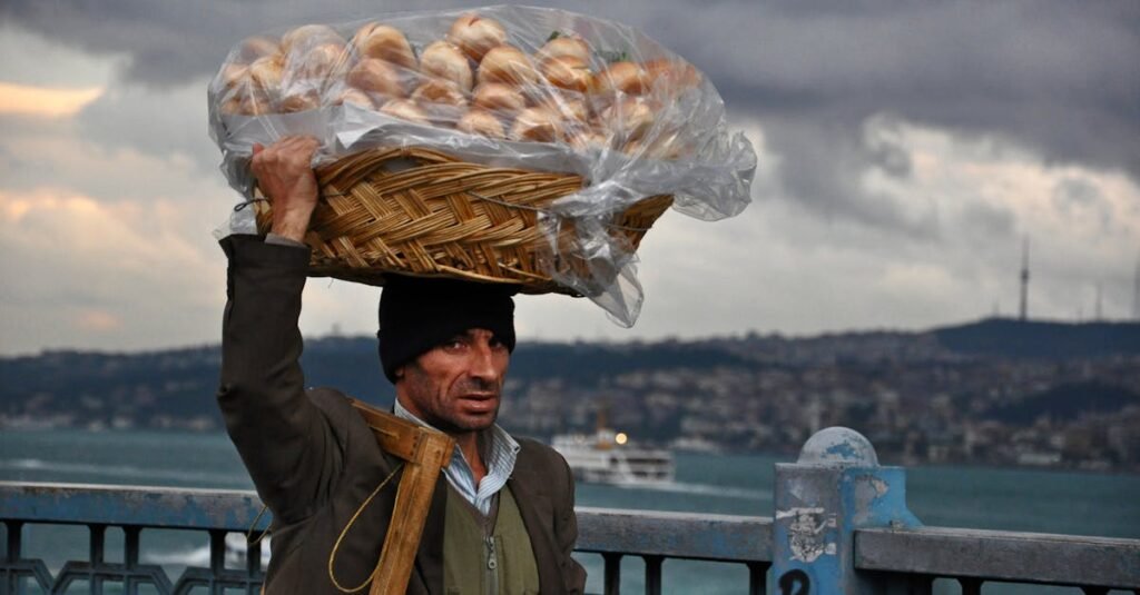 A street vendor in Istanbul carries a basket of bread on his head with a cityscape backdrop.